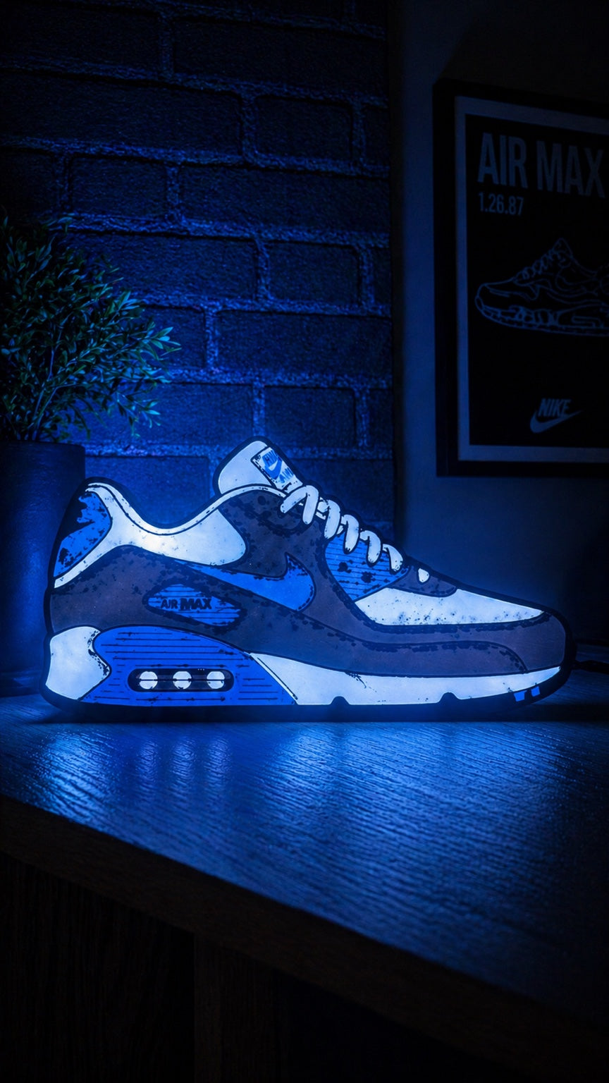 Actual blue, white and black Air Max 90 lightbox illuminated on a desk beside a brick wall.